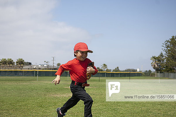 Young boy holding his glove and running across the Tball field