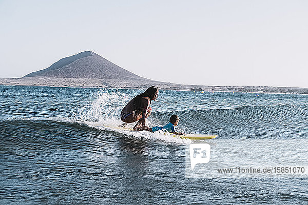 Pulled back view of mother and son surfing a small wave at sea