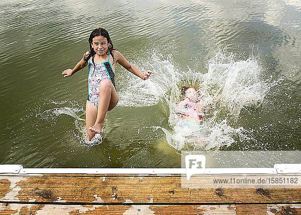 Zwei junge Mädchen in Badeanzügen springen von einem Dock in einen See
