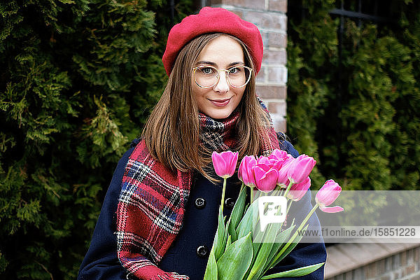 junges französisches tausendjähriges Mädchen in Baskenmütze und Mantel mit Tulpen in den Händen
