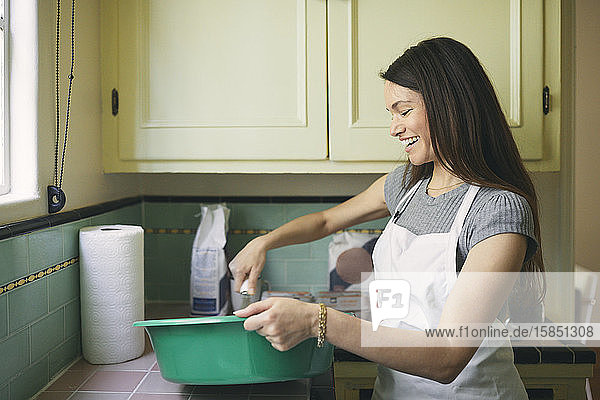 Lächelnde Frau  die in der Küche Essen in einem Behälter verquirlt