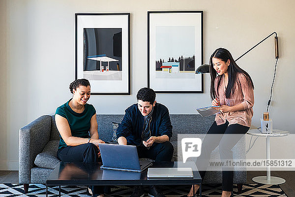 Männliche und weibliche Kollegen diskutieren am Laptop  während sie im Büro auf dem Sofa sitzen