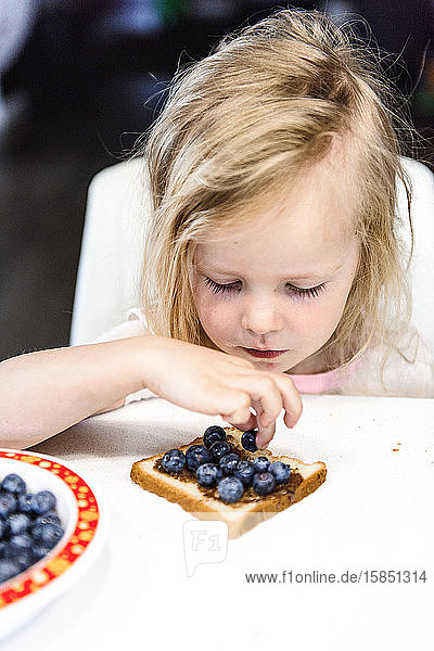 Ein kleines süßes Mädchen isst ihren Frühstückstoast mit Blaubeeren