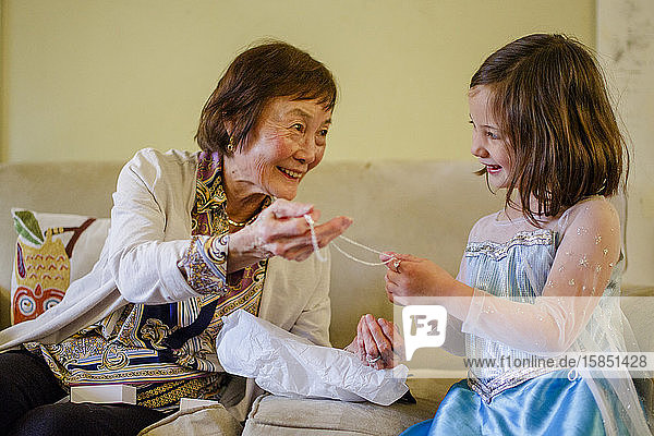 Ein lächelndes Mädchen im Prinzessinnenkostüm öffnet ein Geschenk seiner Großmutter