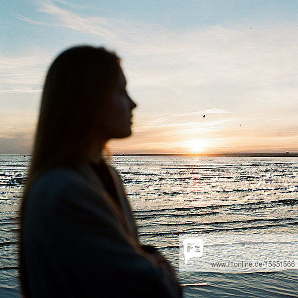 Beautiful woman standing near the sea and enjoying the sunset