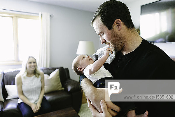 A new father holds his newborn baby son while the mom looks on