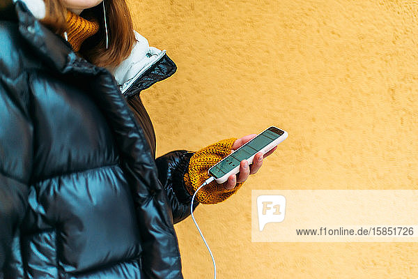 Junge Frau benutzt Smartphone  während sie an gelber Wand steht