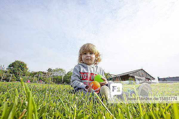 ein kleiner Junge  der auf einer grünen Wiese auf dem Land Bälle spielt und Spaß hat  Caurel Bretagne  Frankreich.