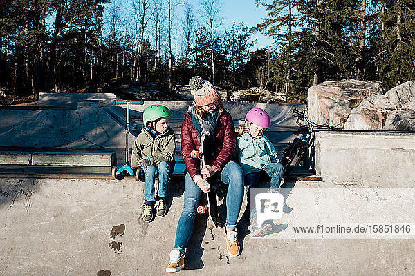 Mama und ihre Kinder spielen in einem Skatepark draußen in der Sonne