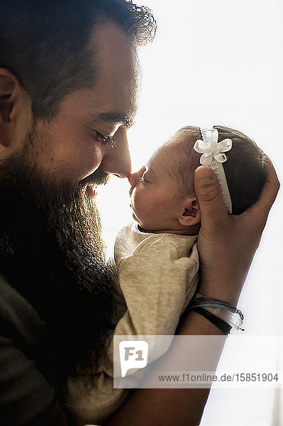 Profile of father and newborn daughter touching noses in pretty light