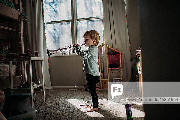 Kleinkind im Schlafzimmer spielt Spielzeug-Trompete