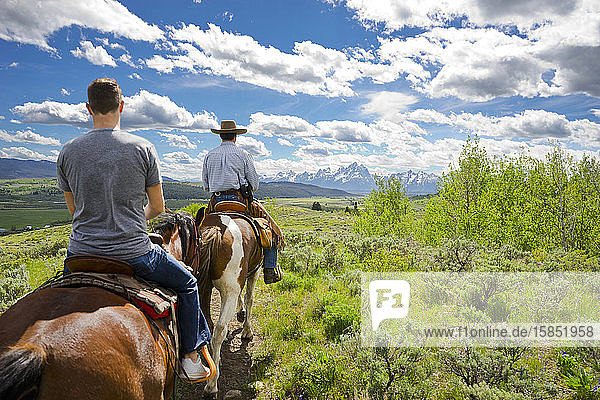 Zwei Männer reiten auf Pferden mit dem Teton-Gebirge in der Ferne