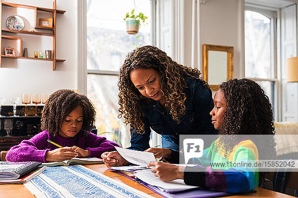 Mutter assistiert Töchtern beim Lernen am Tisch im Wohnzimmer