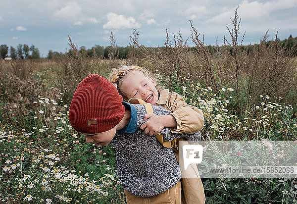 Bruder trägt seine Schwester lachend durch ein Wildblumenfeld