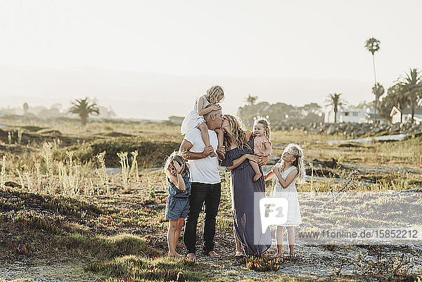 Lifestyle portrait of family with young girls kissing at beach sunset