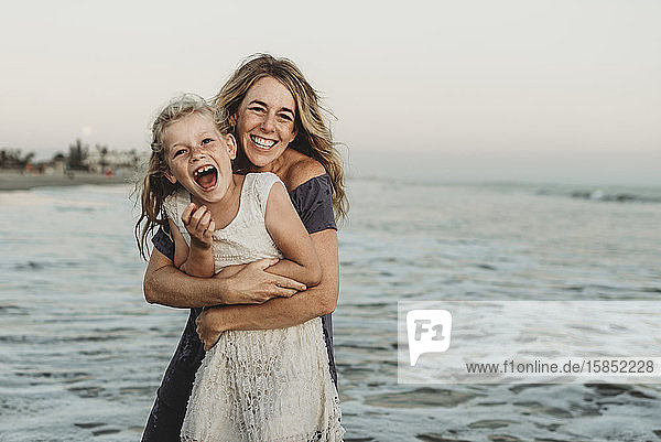 Mutter umarmt junges Mädchen mit Sommersprossen im Meer