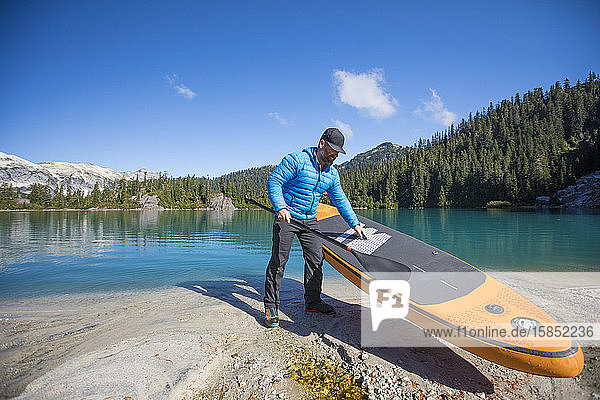 Adventurous man prepares to use SUP on remote alpine lake.