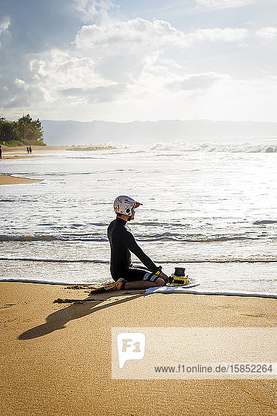 Ein Surffotograf sitzt auf dem Sand und schaut auf das Meer