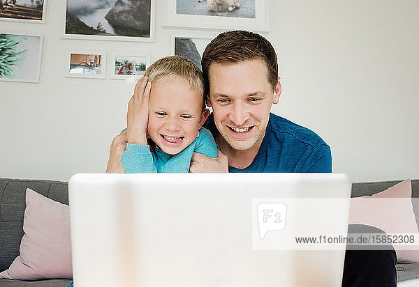 Vater und Sohn lachen zu Hause  während sie zu Hause auf einen Laptop schauen