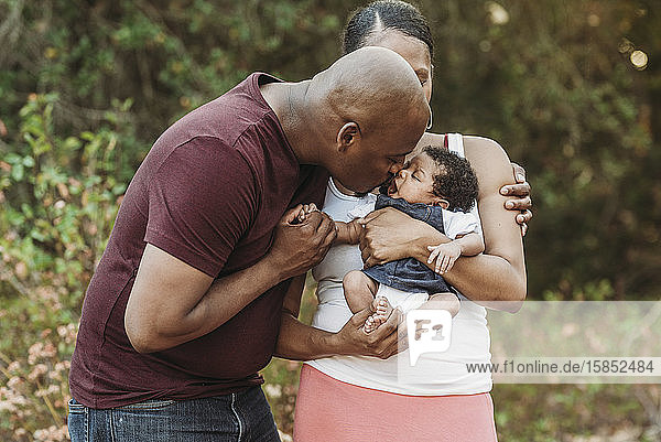 Young Father kissing newborn daughter while mother holds her