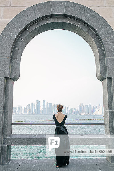 Rückenansicht einer Frau  die das Meer und die Wolkenkratzer von Doha beobachtet