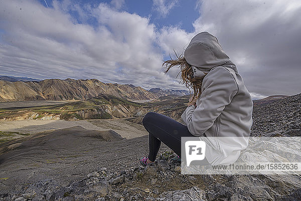 Frau sitzt auf dem Gipfel eines Berges im Wind  in Landmannalaugar