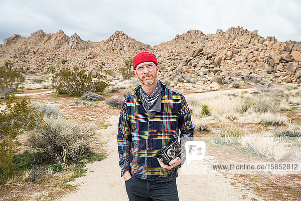 Man in beanie with beard and glasses by far off stone piles in desert