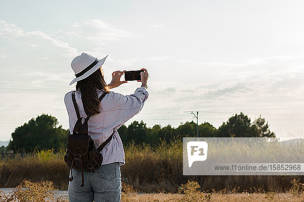 Junge Frau macht ein Foto mit ihrem Smartphone auf einem Feld. Abenteuer  Technik