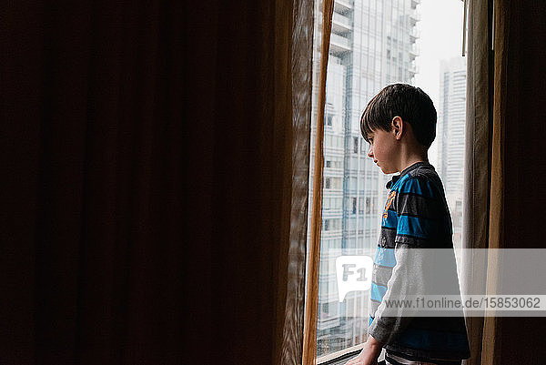 Ein Junge  der aus dem Fenster auf hohe Gebäude der Stadt draußen schaut.