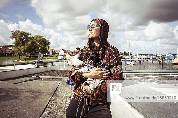 strong woman in sun glasses by boats holds two dogs in sunlight