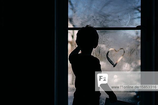 Ein kleiner Junge malt ein Herz auf eine neblige Sturmtür.