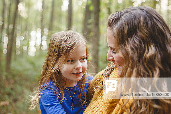 Ein kleines Mädchen schmiegt sich in die Arme seiner Mutter  während sie zusammen lächeln