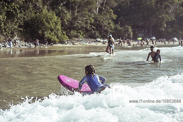 Junges Mädchen fängt Welle auf dem Kinder-Surfbrett schöne Strandbucht