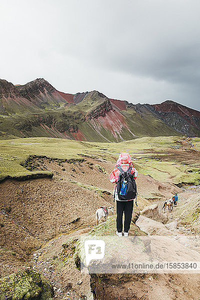 A young woman with a backpack is standing on a hill in Peru