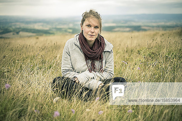 Young woman sitting in grassy meadow looking at camera