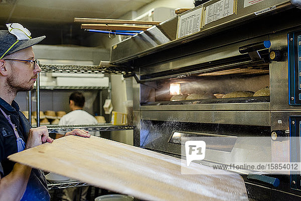 Ein Bäcker stellt in einer Großküche ein Tablett mit Brot in den Ofen