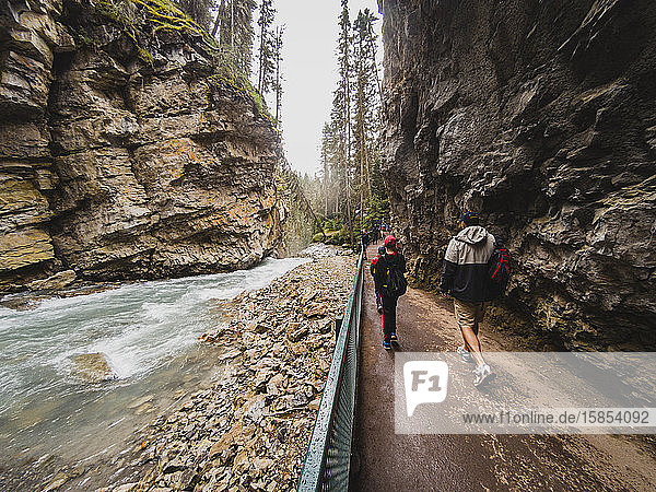 People walking on hiking trail alongside the flowing water in canyon.