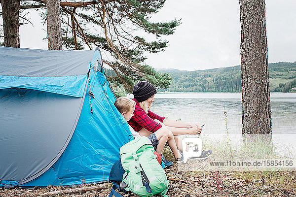 Mutter und Sohn sitzen in einem Zelt und binden Schnürsenkel und lächeln beim Camping
