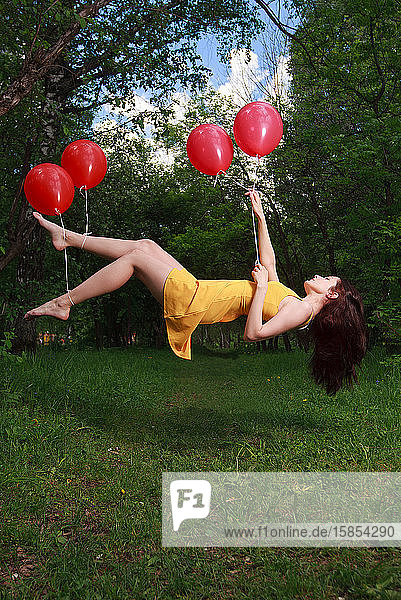 Bezauberndes junges brünettes Mädchen schwebt auf Luftballons in einem Park