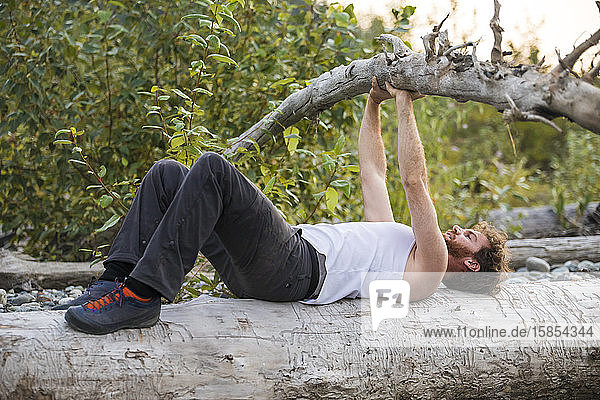 Seitenansicht einer Männerbank beim Drücken eines umgefallenen Baumes während eines Trainings im Freien.