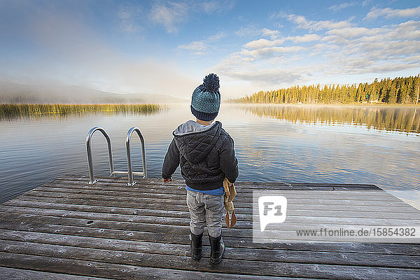 Junge steht am Dock und schaut auf einen ruhigen See