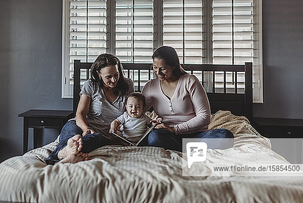 Happy moms reading book in bed with laughing baby