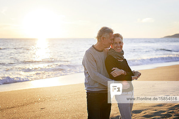 Zärtliches älteres Ehepaar  das bei Sonnenuntergang am Strand steht