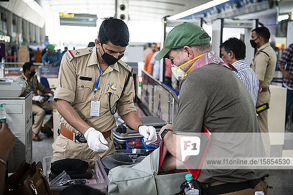 Ariport-Sicherheitspersonal am Flughafen Khajuraho  Madhya Pradesh  Indien  durchsucht den Inhalt des Gepäcks eines Passagiers  wobei alle abgebildeten Personen Gesichtsmasken als Schutzmaßnahme tragen