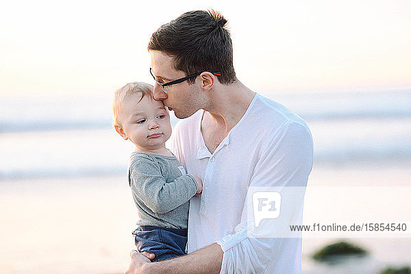 Ein junger Vater gibt seinem Sohn auf dem Tempel am Strand einen Kuss.