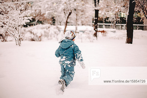 Rear view of boy running in snow covered field in park in winter