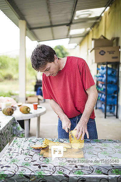 Junger Mann schneidet frische  biologische Ananas auf einem Holzschneidebrett.