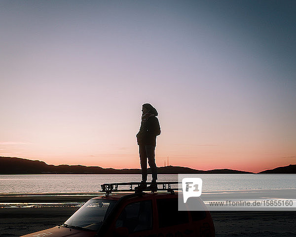Beautiful woman in glasses stands on the roof of the car