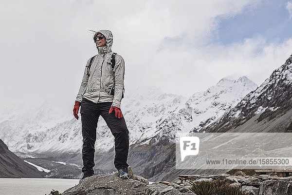 cold woman stands on rock while hiking to Hooker Valley New Zealand