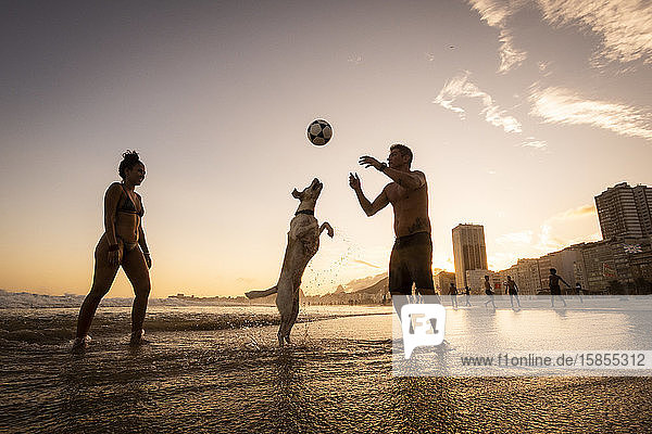 Couple playing soccer with dog on the water front in Copacabana Beach